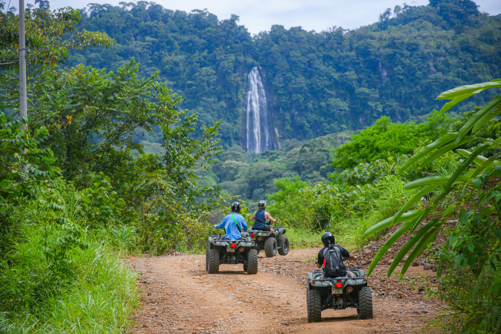 ATV riders on a trail beneath a waterfall